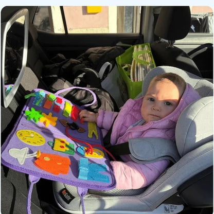 A little girl playing with the busy board in her car seat